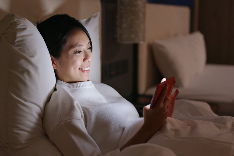 mulher usando o celular na cama.