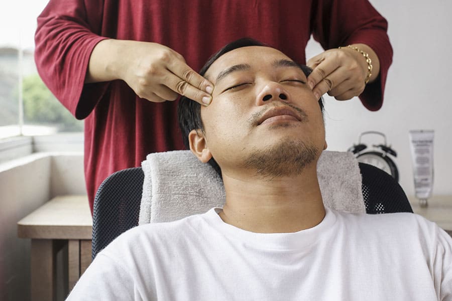 Esteticista fazendo massagem facial pressionando o rosto próximo aos olhos.