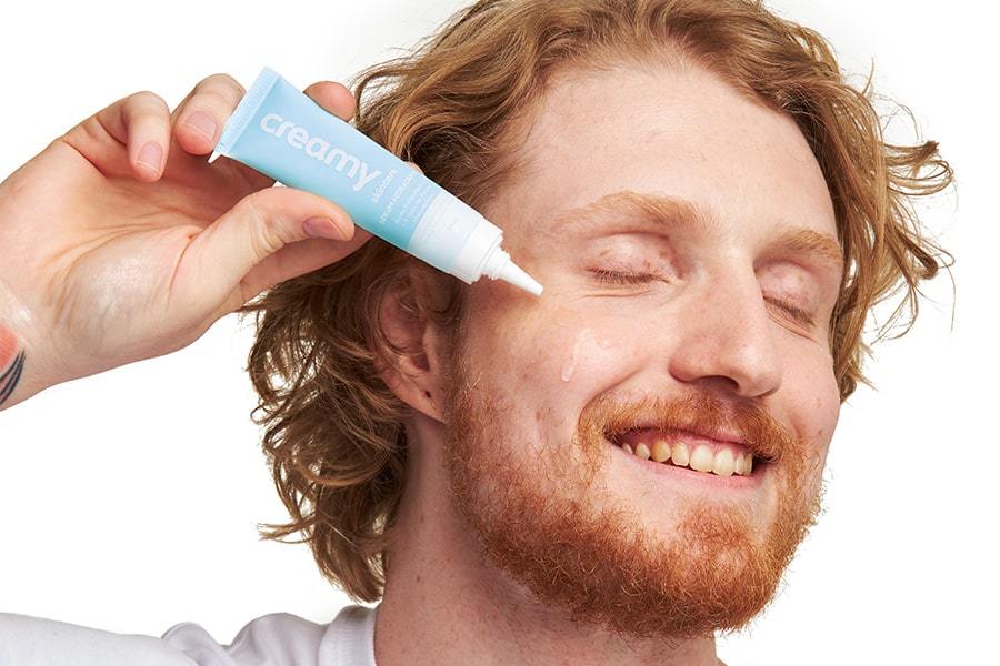 Homem ruivo aplicando o Sérum Hidratante Facial da Creamy na bochecha.