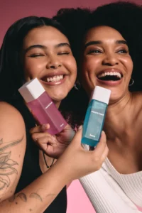 Duas mulheres, com seus rostos bem próximos, cada uma segurando uma fragrância Creamy e sorrindo.